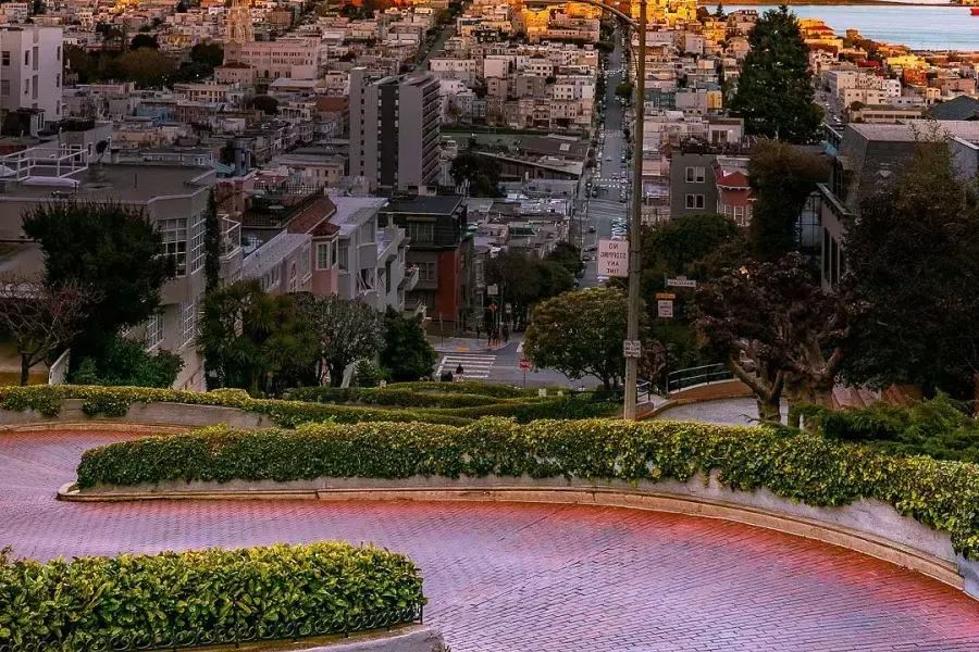 Curvas da Lombard Street com Coit Tower ao longe durante sunset .